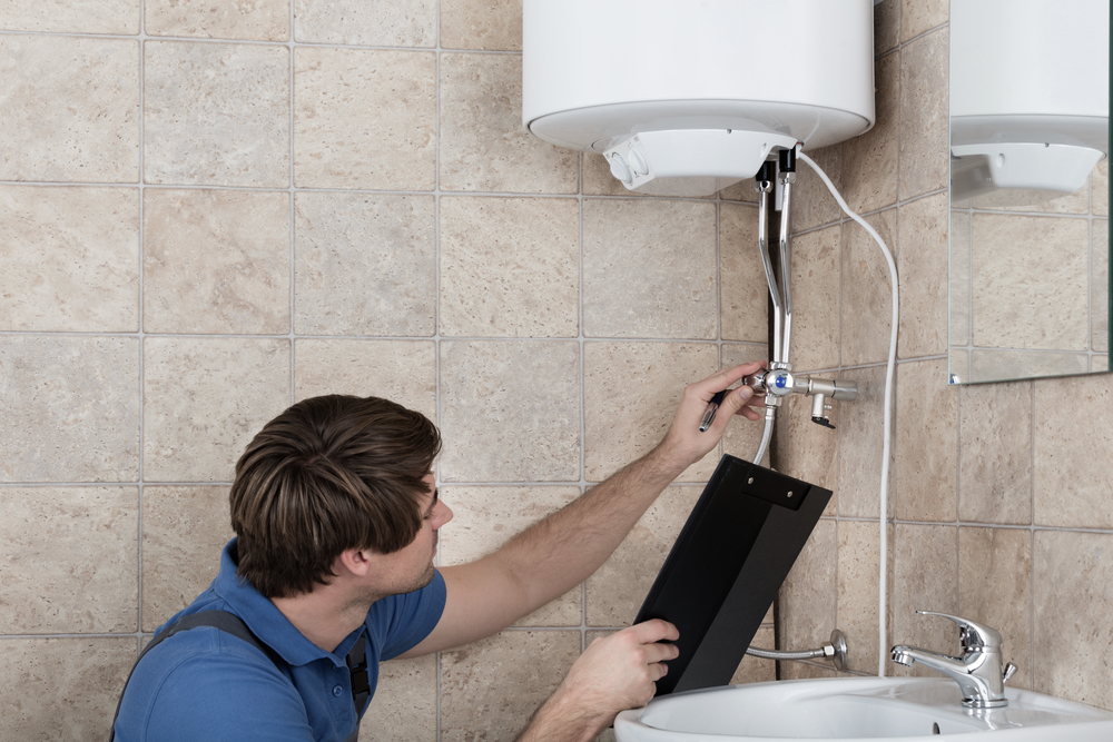 Male Plumber Checking Electric Boiler And Holding Clipboard At Home