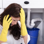 Sad Young Woman Calling Plumber In Front Of Water Leaking
