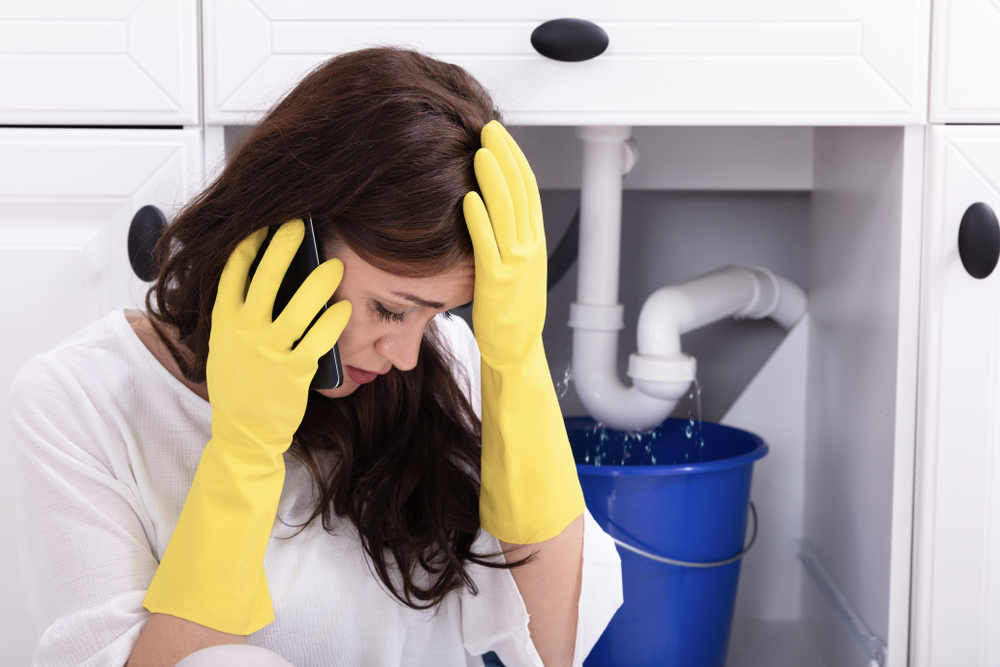 Sad Young Woman Calling Plumber In Front Of Water Leaking