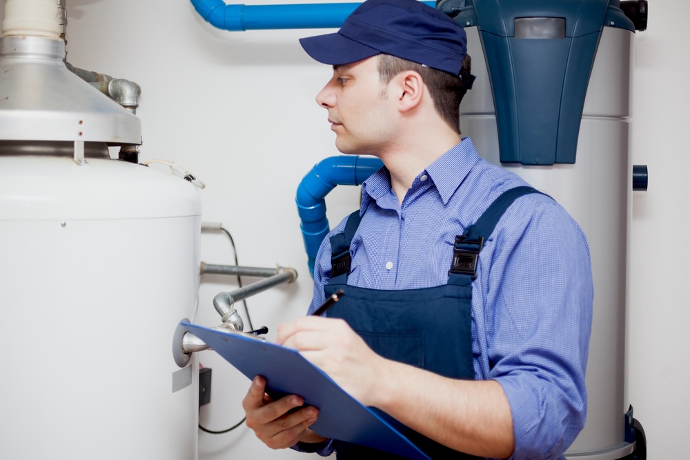 A plumber wearing a blue cab and blue shirt doing a plumbing diagnosis on a water tank